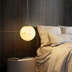 Clérachic Alabaster Globe Pendant Light glowing beside a dark timber headboard, throwing warm light across beige bedlinen.