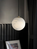 Clérachic Alabaster Globe Pendant Light in cool white with grey veining, hung beside black slatted panelling and a leaning artwork.