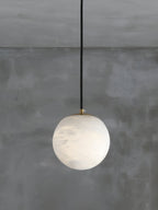 The Clérachic Alabaster Globe Pendant Light seen from further back, brass disc on top and faint grey veining across the stone.