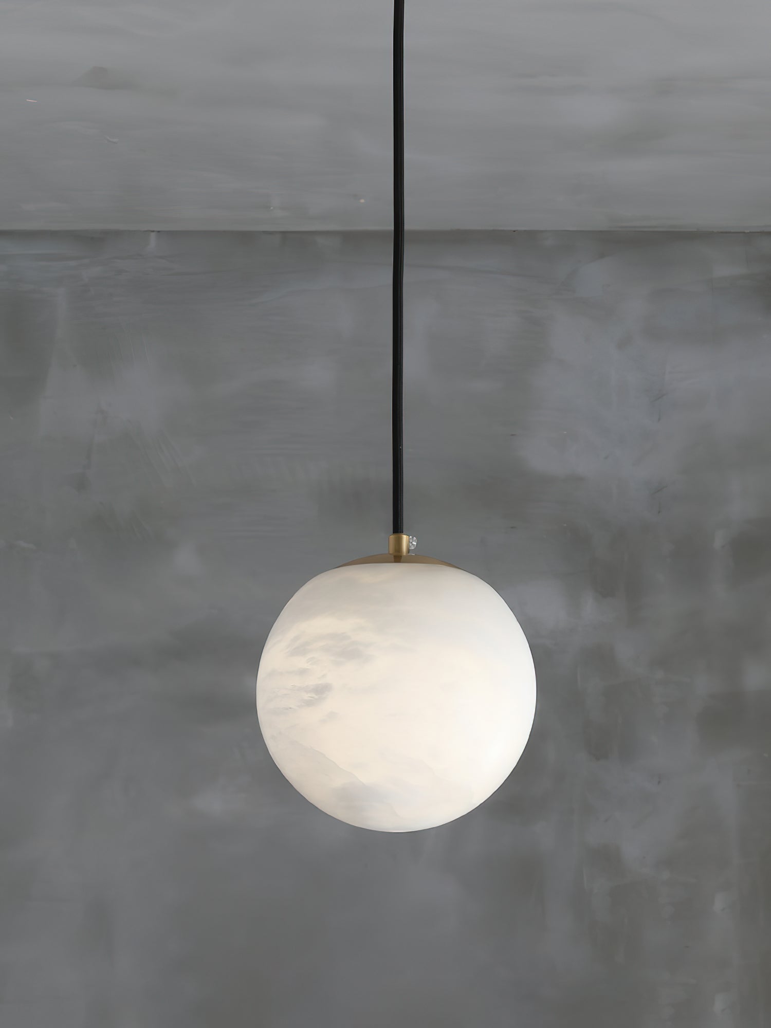 The Clérachic Alabaster Globe Pendant Light seen from further back, brass disc on top and faint grey veining across the stone.