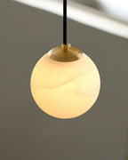 Detail of the brass collar and cord fixing on the Clérachic Alabaster Globe Pendant Light, the lit stone glowing beneath it.