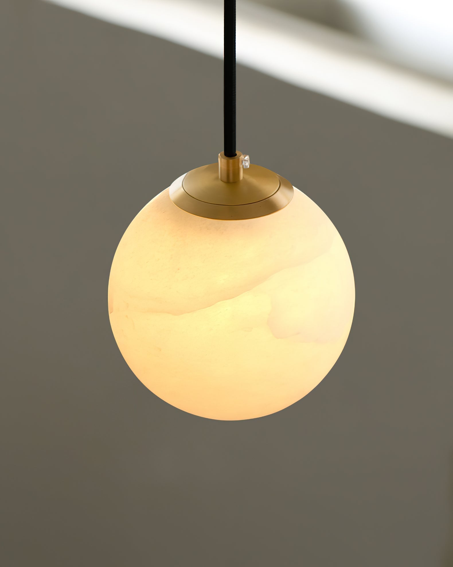 Detail of the brass collar and cord fixing on the Clérachic Alabaster Globe Pendant Light, the lit stone glowing beneath it.