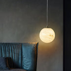 Clérachic Alabaster Globe Pendant Light lit beside a teal velvet headboard, casting a warm pool on the dark bedroom wall.