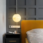 Clérachic Alabaster Globe Pendant Light hanging over a black nightstand beside a mustard headboard and grey panelled wall.