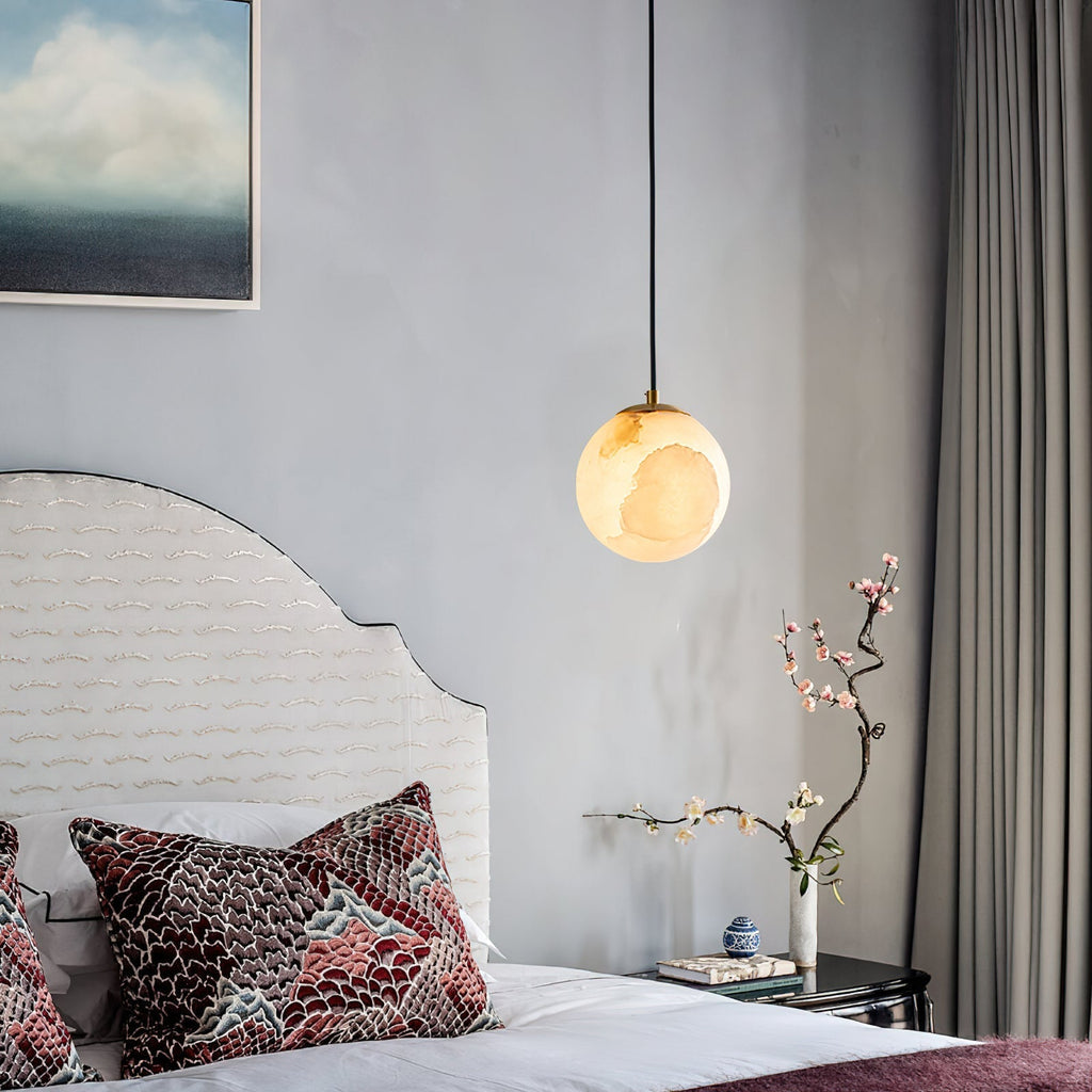 Clérachic Alabaster Globe Pendant Light on a long black cord beside a scalloped headboard and a branch of pink blossom.