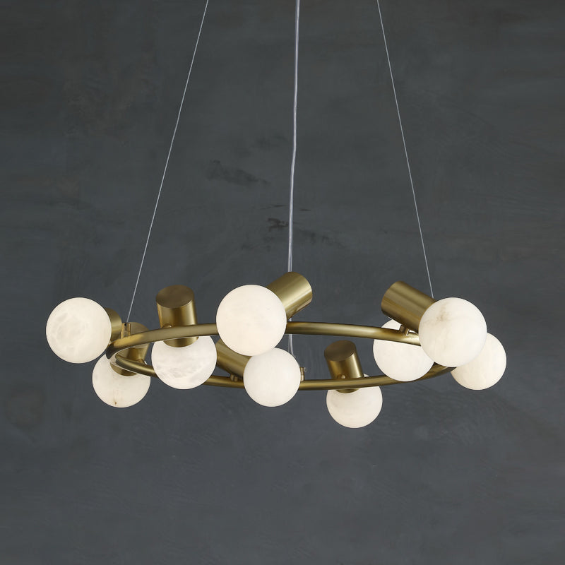The brass ring of the Clérachic Alabaster Globe Ring Chandelier seen at an angle, chalk-white globes unlit in a grey room.