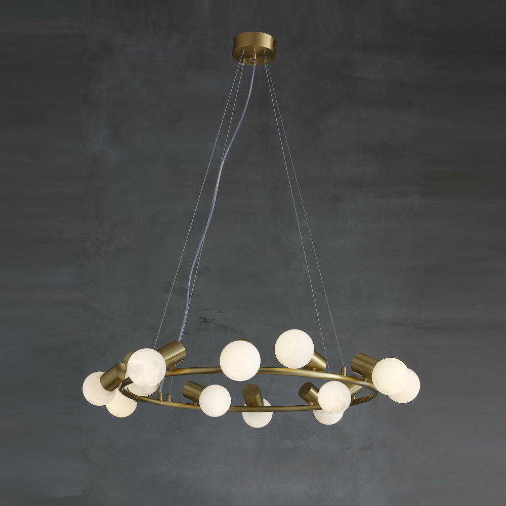 Clérachic Alabaster Globe Ring Chandelier hung low in a dim grey room, the brass ring catching light while the globes stay off.