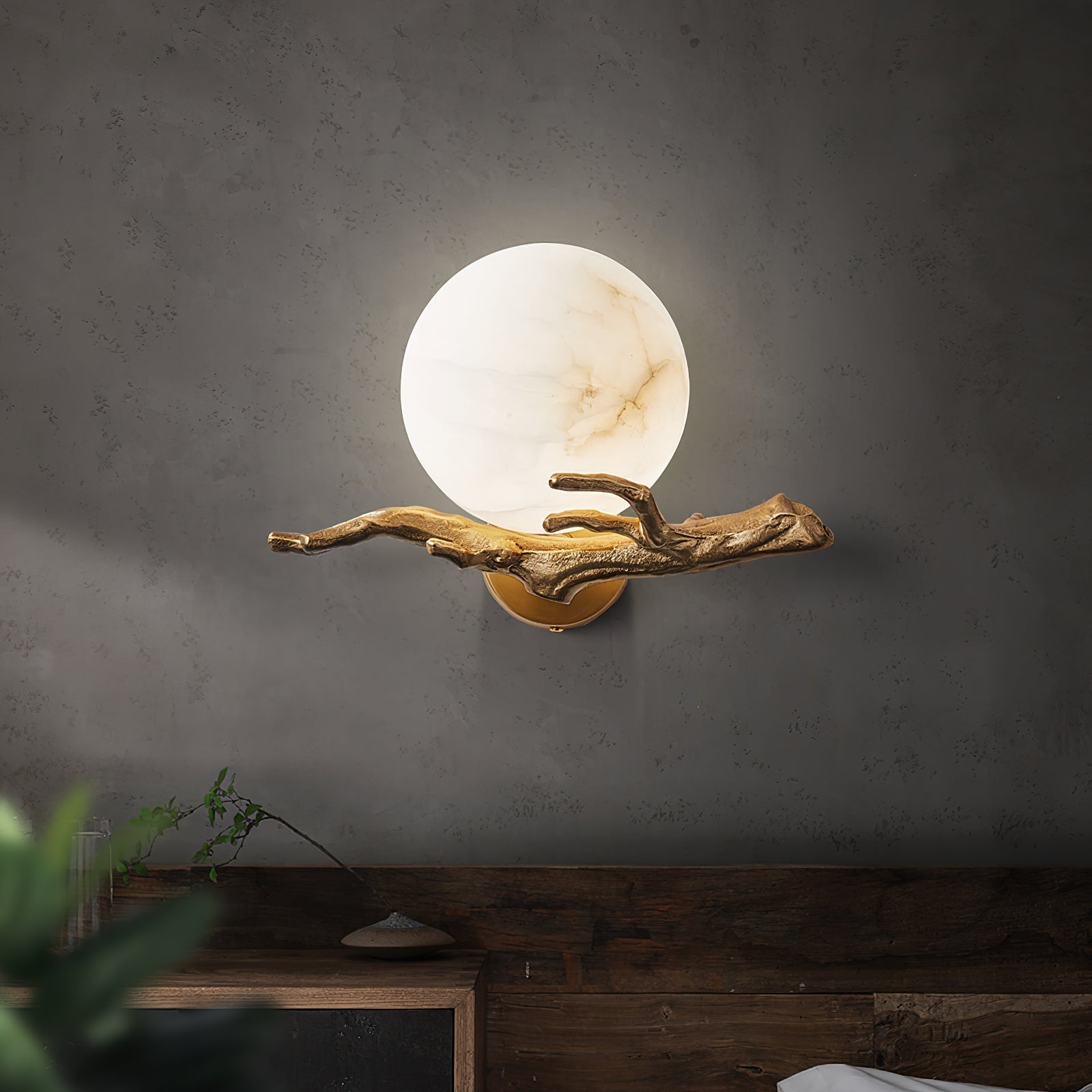 The Clérachic Alabaster Globe Wall Sconce lit on a grey plaster wall above a reclaimed wood sideboard, the stone glowing honey-warm.