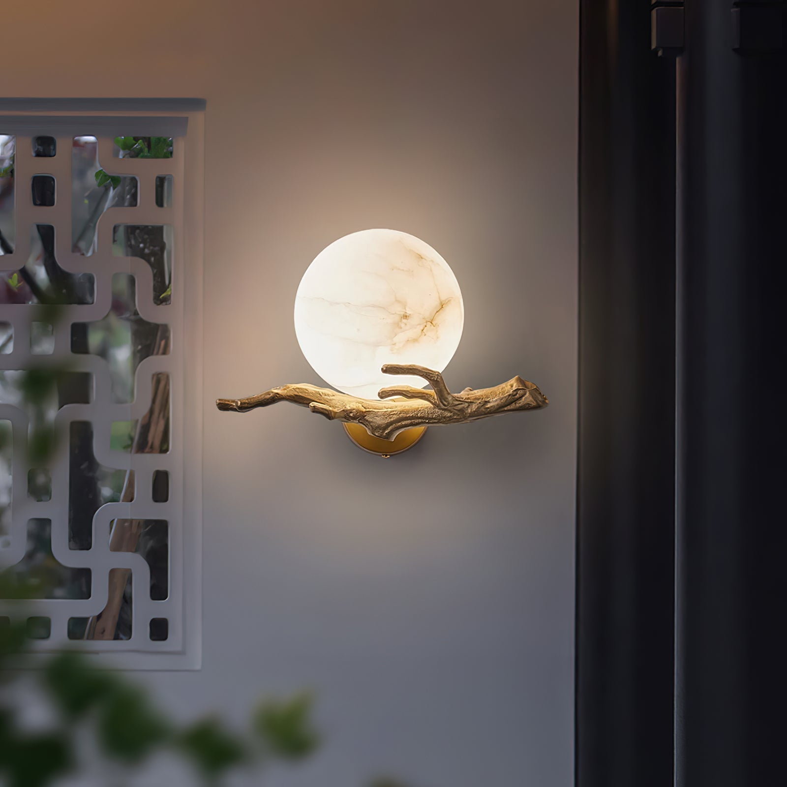Clérachic Alabaster Globe Wall Sconce glowing beside a white lattice screen at dusk, warm light spilling around the veined globe.