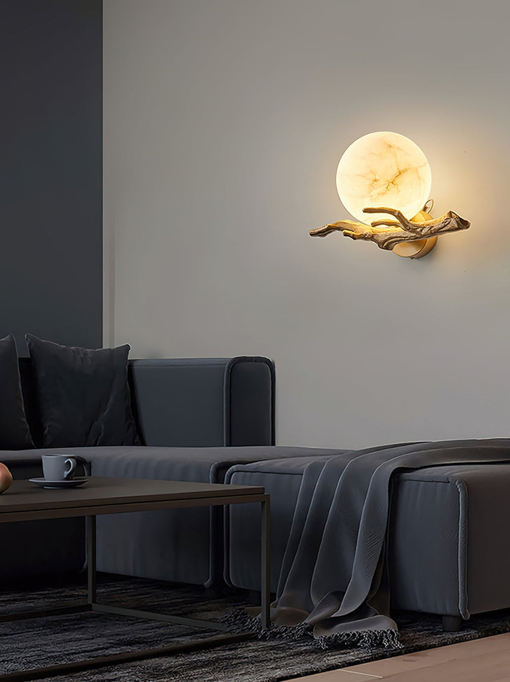 The Clérachic Alabaster Globe Wall Sconce lighting a corner above a charcoal sofa, its warm globe the only light in the room.