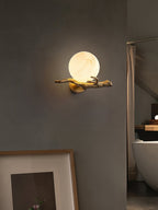 Clérachic Alabaster Globe Wall Sconce on a grey plaster wall above a leaning framed print, the lit stone reading like a small moon.