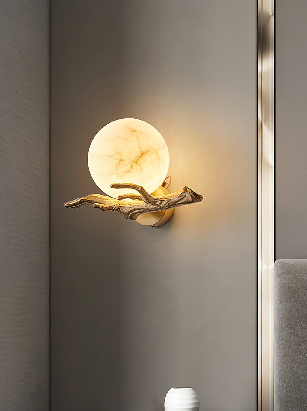 Clérachic Alabaster Globe Wall Sconce on a narrow grey pier, the alabaster veining lit from within and the arm reaching left.