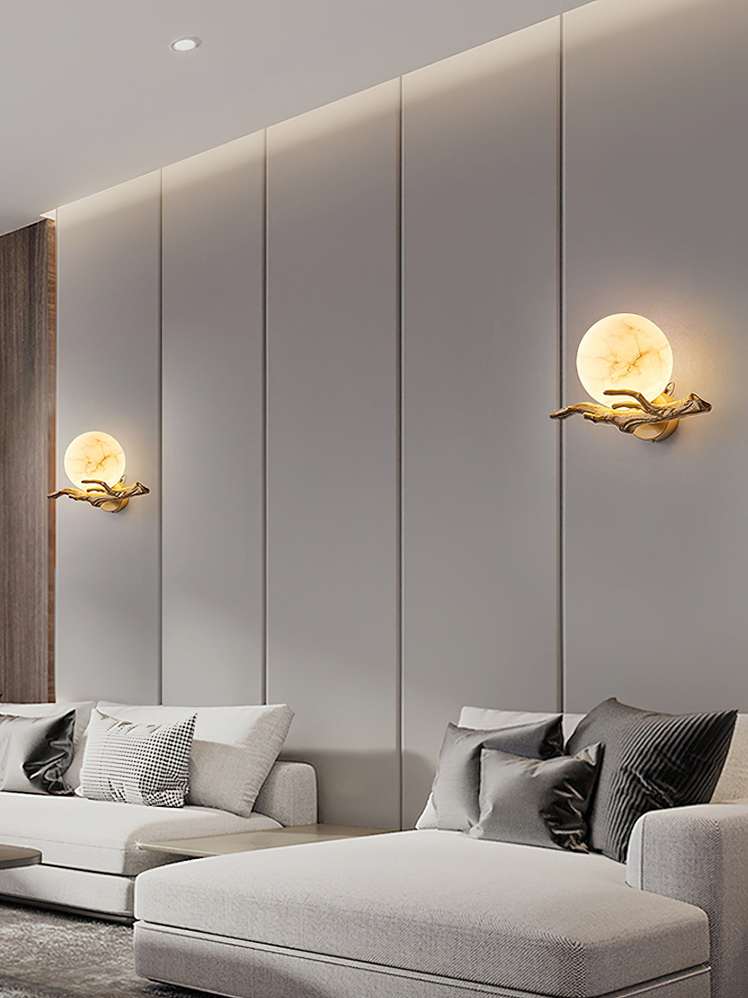 A pair of Clérachic Alabaster Globe Wall Sconces spaced along a panelled wall above a pale sofa, both globes lit soft gold.