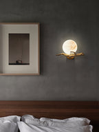 Clérachic Alabaster Globe Wall Sconce glowing on a deep grey bedroom wall next to a framed print, above crisp white bedlinen.