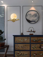 The Clérachic Alabaster Globe Wall Sconce on a white panelled wall above a painted chest, its globe echoing a round ink painting.