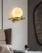 Clérachic Alabaster Globe Wall Sconce lit above a bedside table, the cast brass branch stretching wide across a pale grey wall.
