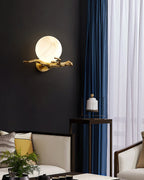 Clérachic Alabaster Globe Wall Sconce lit on a matte black wall beside deep blue curtains, the stone glowing above a sitting area.