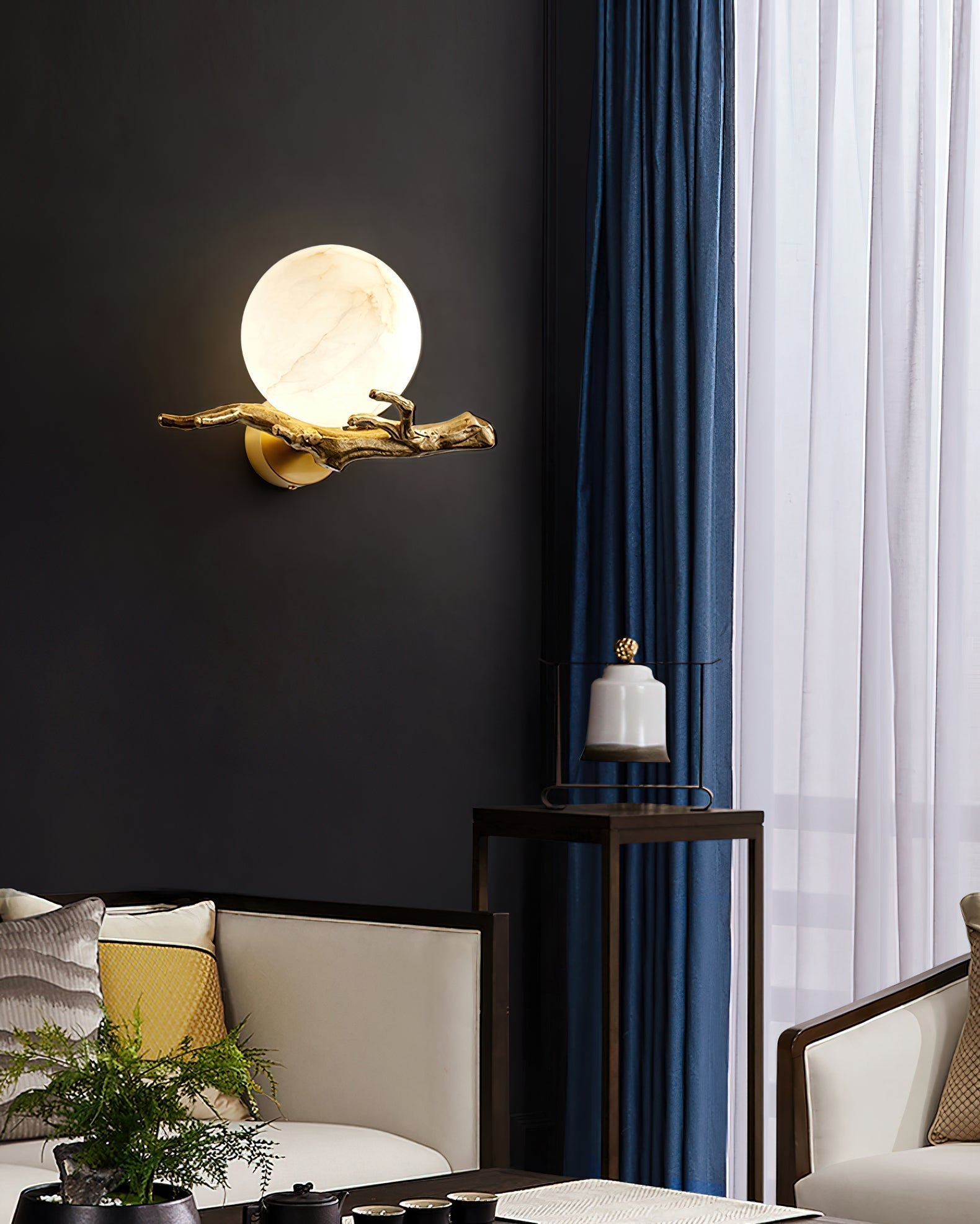 Clérachic Alabaster Globe Wall Sconce lit on a matte black wall beside deep blue curtains, the stone glowing above a sitting area.