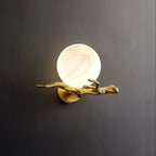The Clérachic Alabaster Globe Wall Sconce lit on a dark grey ground, warm light bleeding out around the veined alabaster ball.