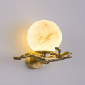 The Clérachic Alabaster Globe Wall Sconce lit at an angle, veining running across the stone while the brass arm catches the light.