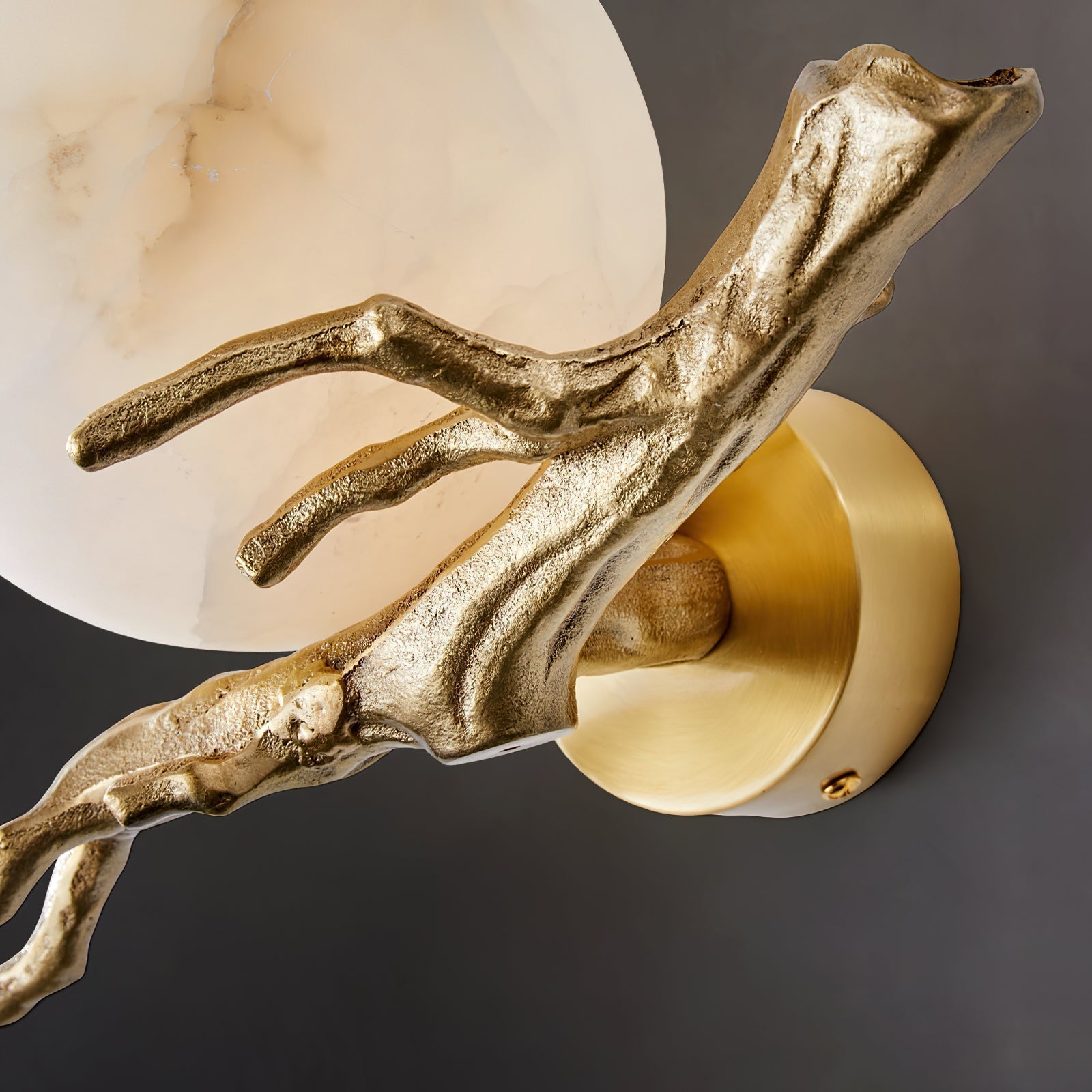 Close detail of the Clérachic Alabaster Globe Wall Sconce, where the cast branchlets meet the round brushed brass wall plate.