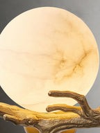 The Clérachic Alabaster Globe Wall Sconce close up and lit, the alabaster warmed to honey with brass branchlets crossing its face.