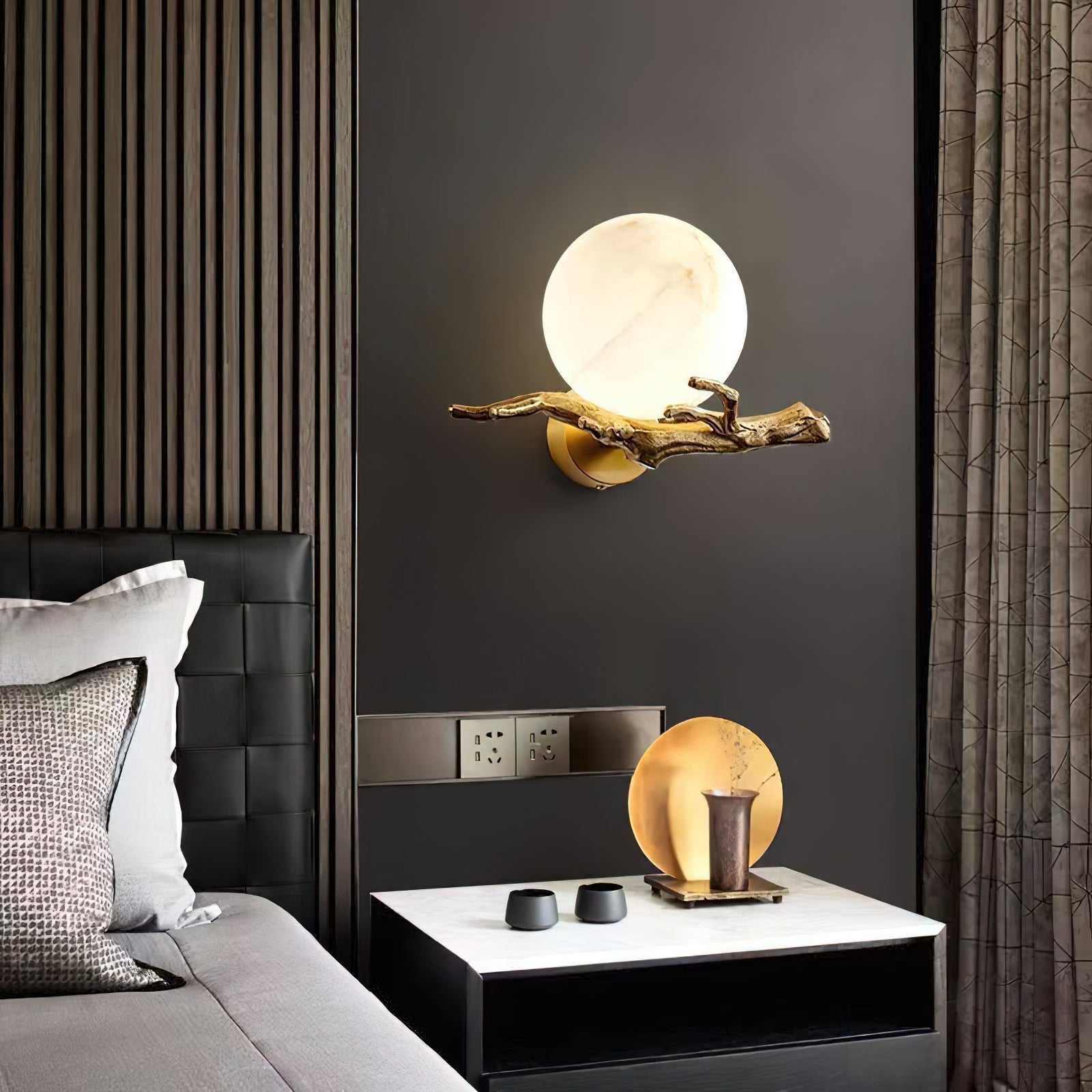 Clérachic Alabaster Globe Wall Sconce on a dark bedroom wall above a nightstand, casting a soft pool beside a leather headboard.