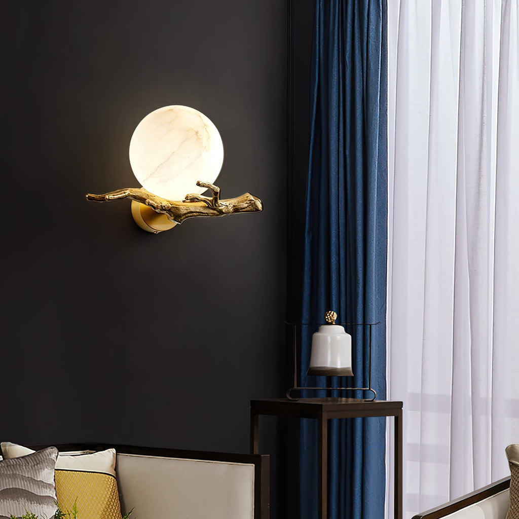 Clérachic Alabaster Globe Wall Sconce alone on a black wall, its warm globe and brass branch reading as wall sculpture after dark.
