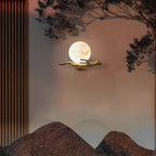 The Clérachic Alabaster Globe Wall Sconce lit at dusk on a textured wall, real branches overhead echoing the cast brass arm.