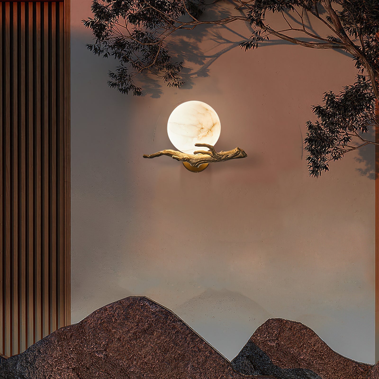 The Clérachic Alabaster Globe Wall Sconce lit at dusk on a textured wall, real branches overhead echoing the cast brass arm.
