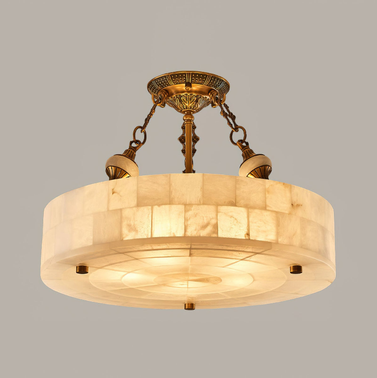 Front view of the alabaster block drum on this Clérachic ceiling light, lit warm against a mid-grey backdrop, with brass chains above.