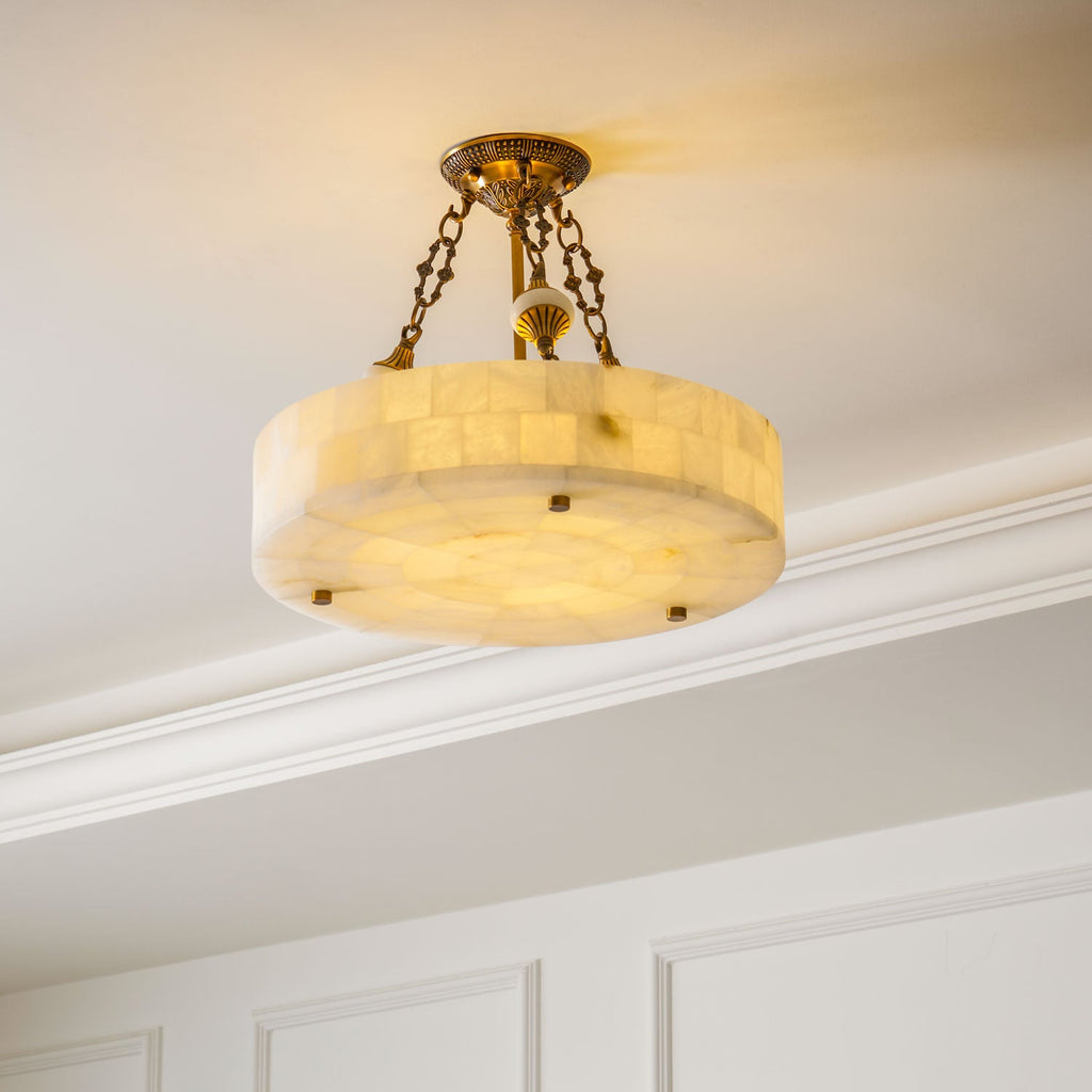 Clérachic alabaster ceiling light lit warm beneath a white ceiling with deep cornice moulding, its brass chains reaching the canopy.