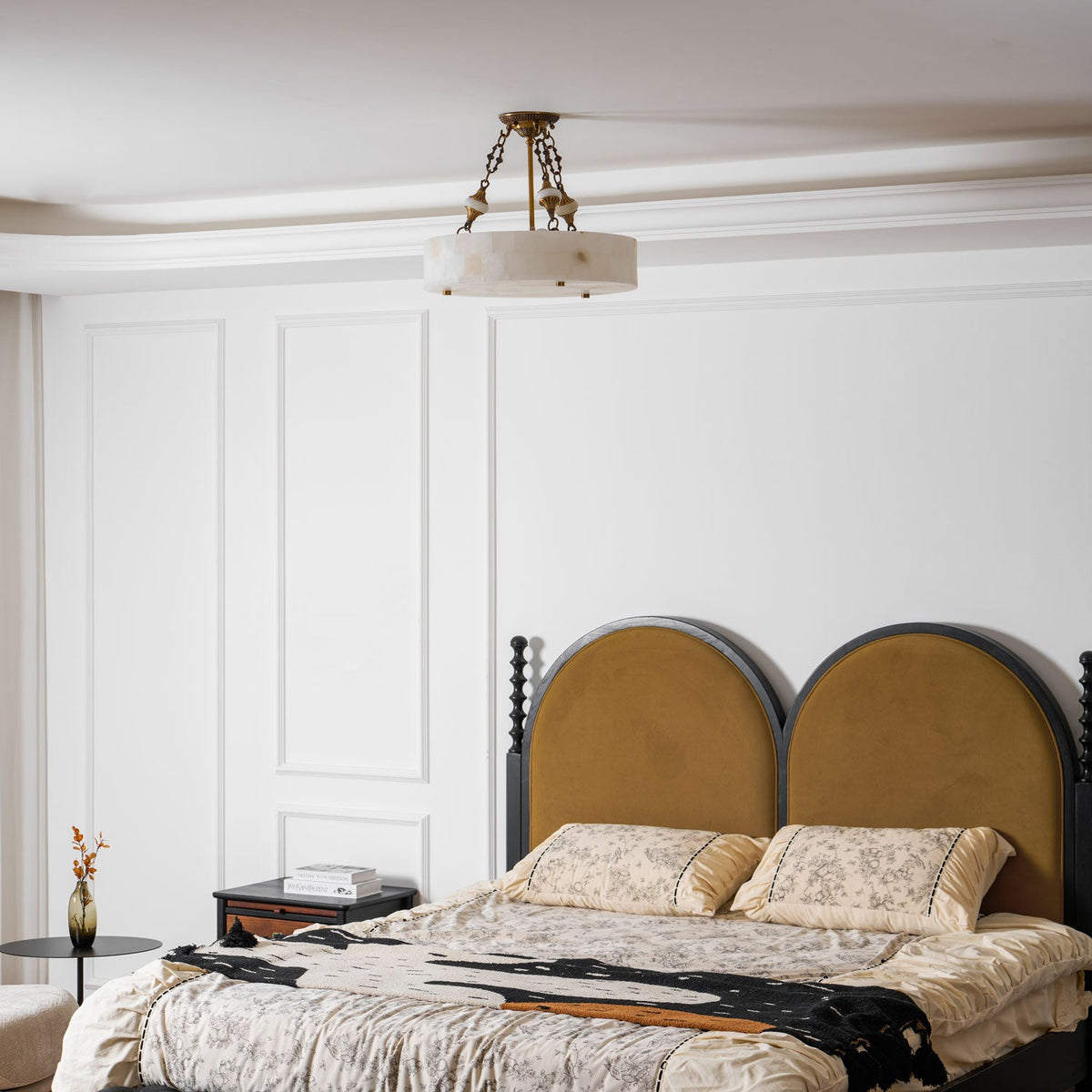 Wide room view with a small Clérachic alabaster ceiling light high above a bed with an arched mustard headboard and white wall panelling.