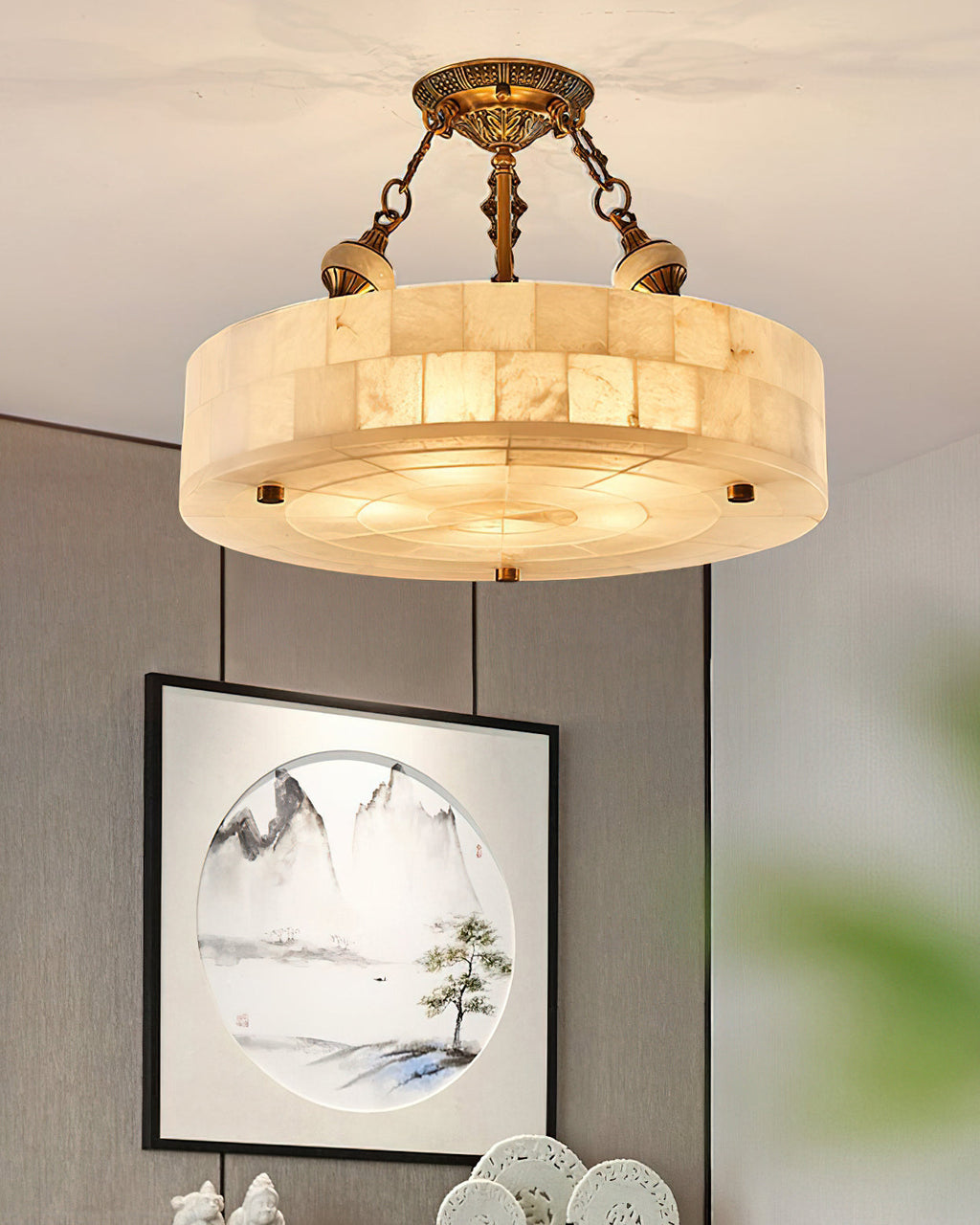 This Clérachic ceiling light hangs in front of a grey wall, its alabaster blocks lit from inside, with a framed landscape print below.