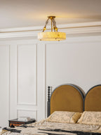 Vertical view of a Clérachic alabaster ceiling light lit warm above white wall panelling and an arched mustard headboard.