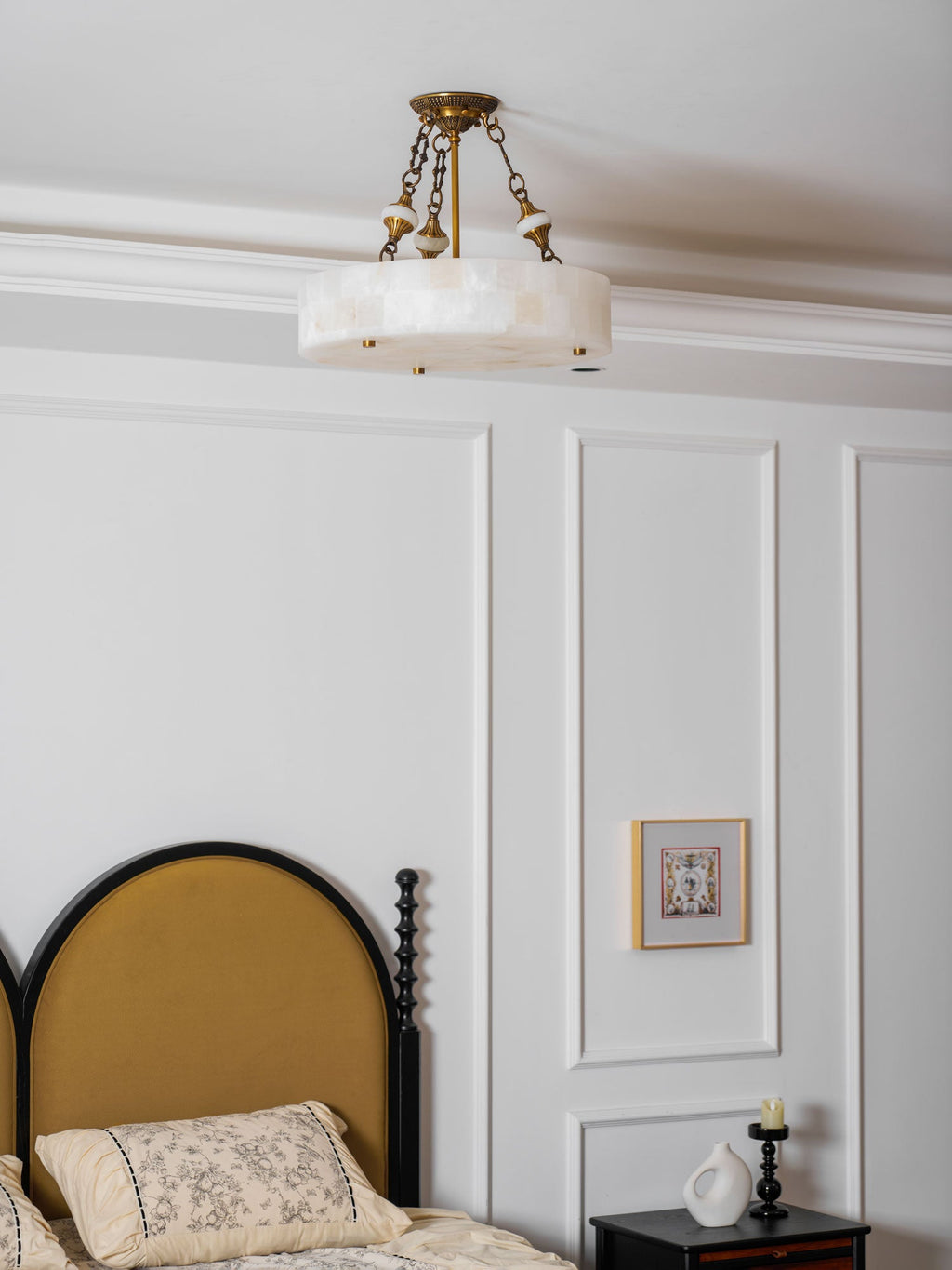 Unlit Clérachic alabaster ceiling light below a white cornice, with an arched mustard headboard and a small framed picture beneath.