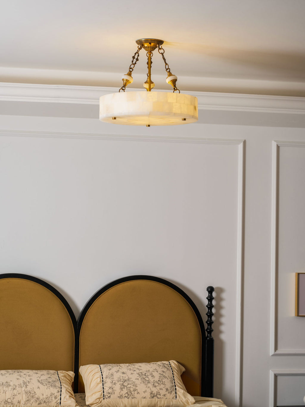 Clérachic alabaster ceiling light centred above a double bed, its brass chains clear against white panelled walls.