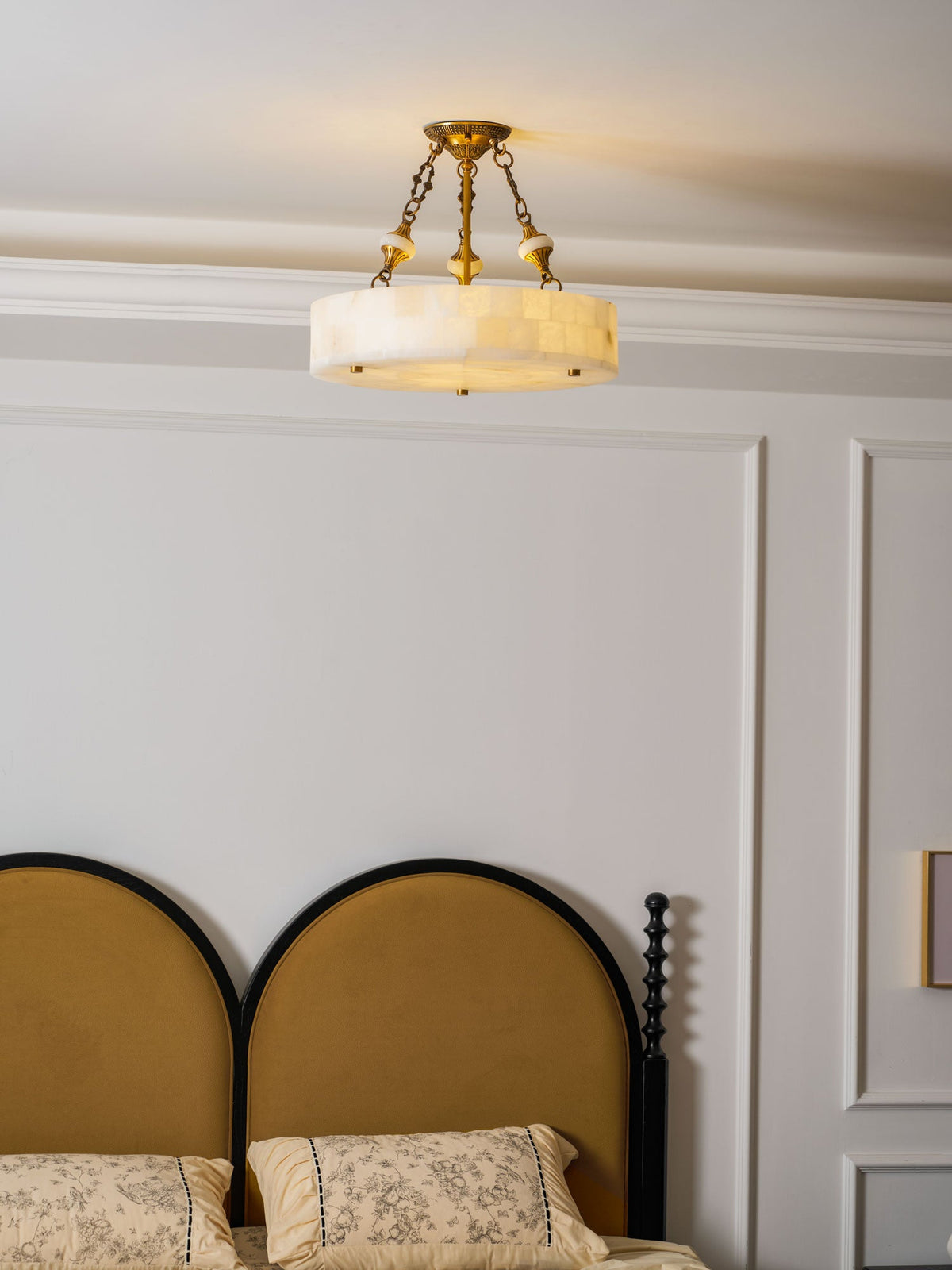 Clérachic alabaster ceiling light centred above a double bed, its brass chains clear against white panelled walls.
