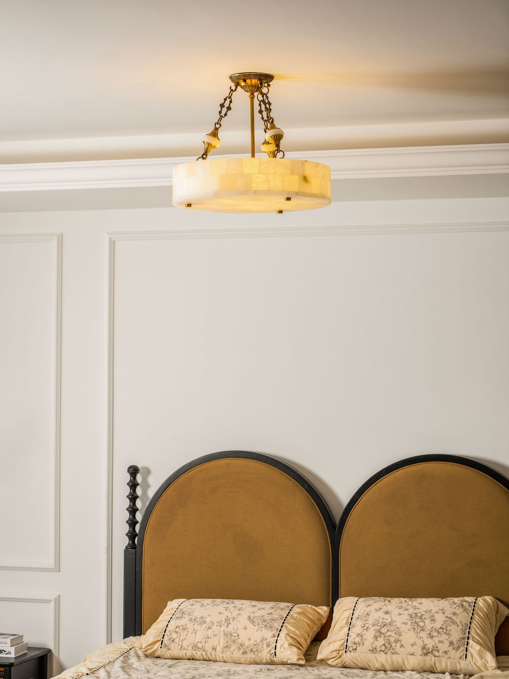 Warmly lit Clérachic alabaster ceiling light close to the cornice, above a bed with two arched mustard headboards.