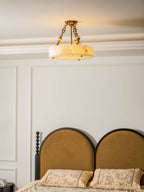 Warmly lit Clérachic alabaster ceiling light close to the cornice, above a bed with two arched mustard headboards.