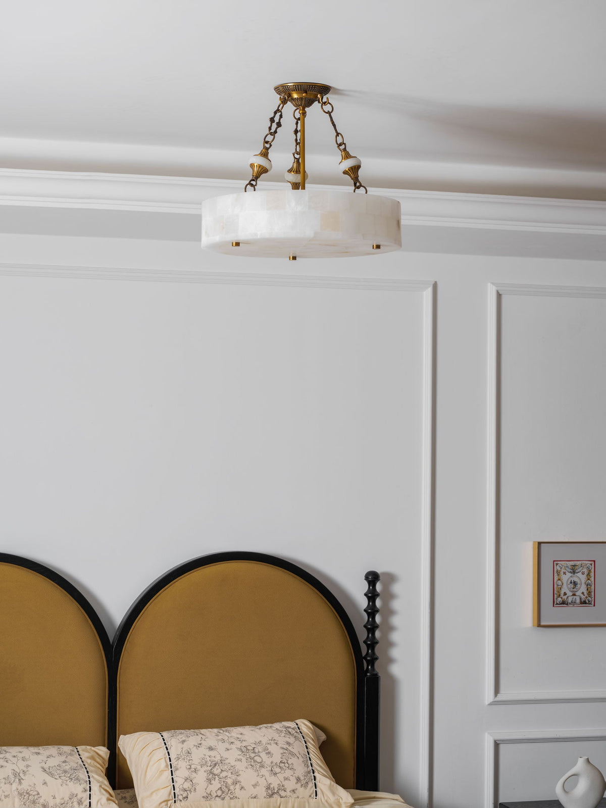 Pale alabaster drum of this Clérachic ceiling light seen from below, with white wall panels and a bedside vase in view.