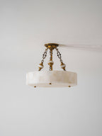 Slim alabaster drum Clérachic ceiling light with three chains and brass studs, photographed against a pale grey wall.