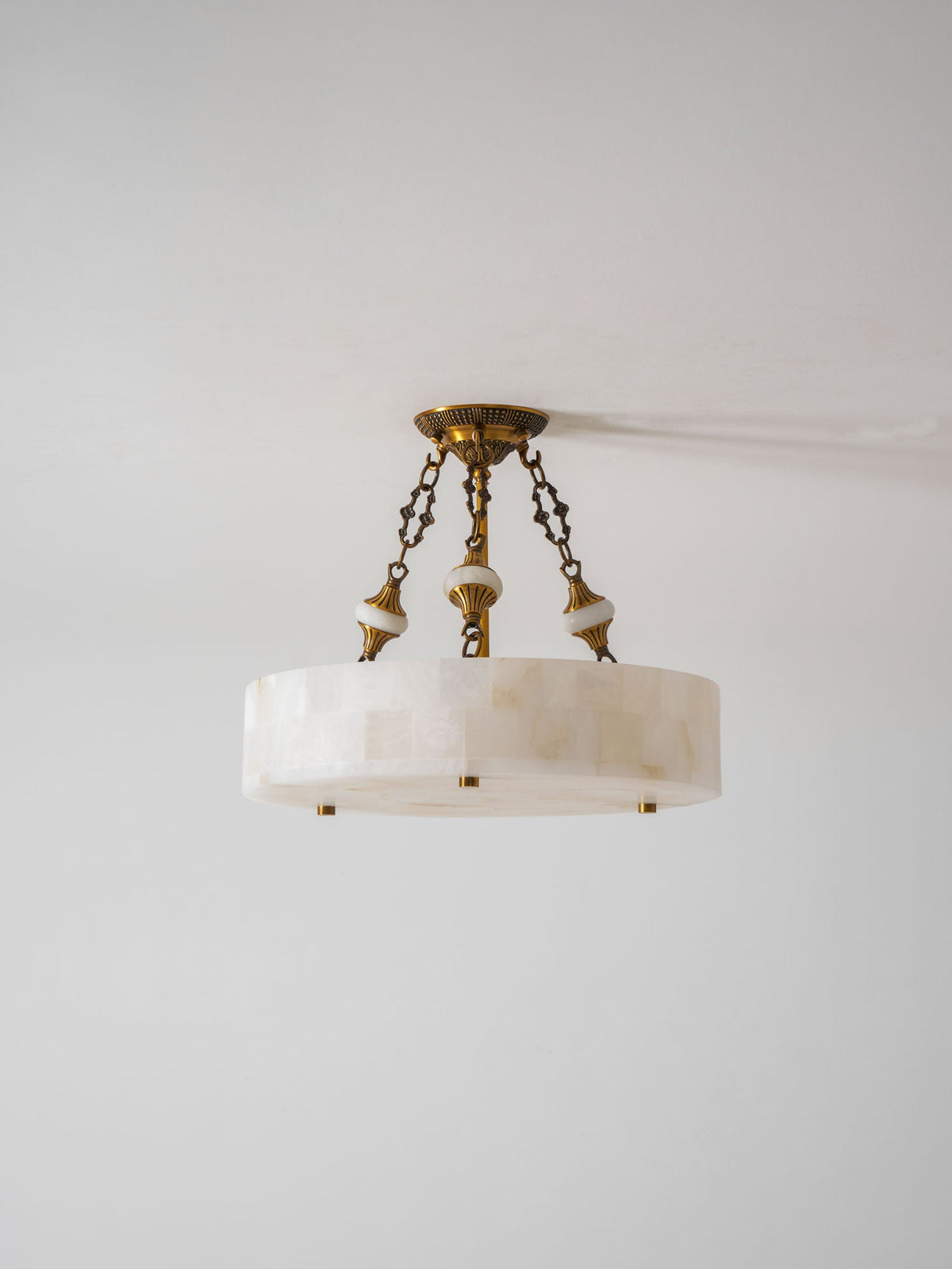 Slim alabaster drum Clérachic ceiling light with three chains and brass studs, photographed against a pale grey wall.