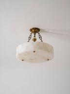 Angled view from below of the alabaster block drum on this Clérachic ceiling light, with its antique brass chains and canopy.