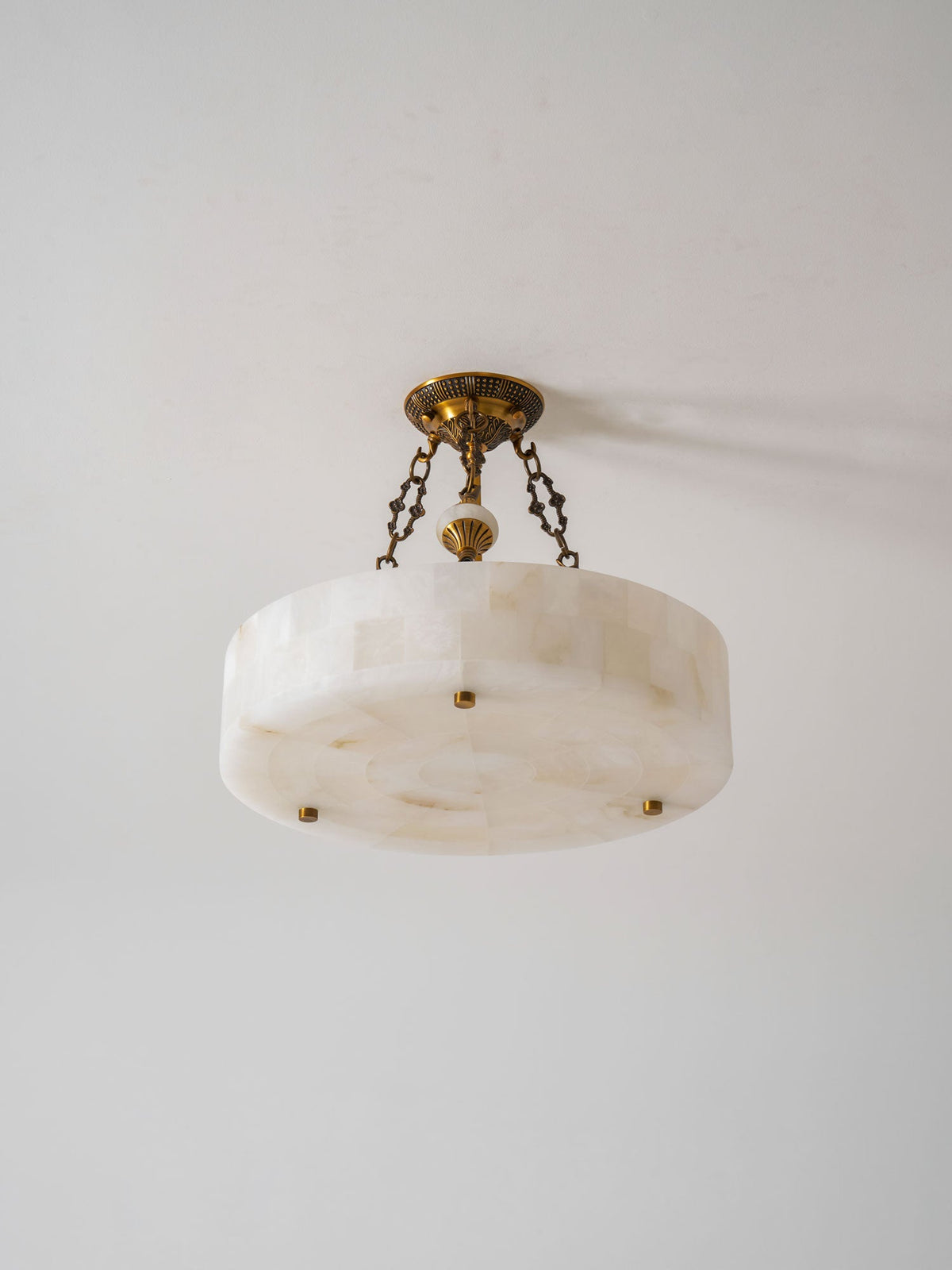 Angled view from below of the alabaster block drum on this Clérachic ceiling light, with its antique brass chains and canopy.