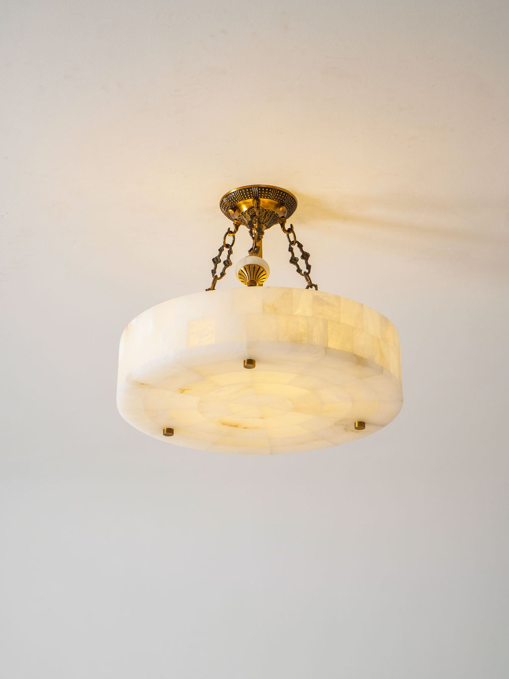 Clérachic alabaster ceiling light seen from slightly above, its blocks of stone glowing softly against a plain light wall.