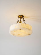 Clérachic alabaster ceiling light seen from slightly above, its blocks of stone glowing softly against a plain light wall.