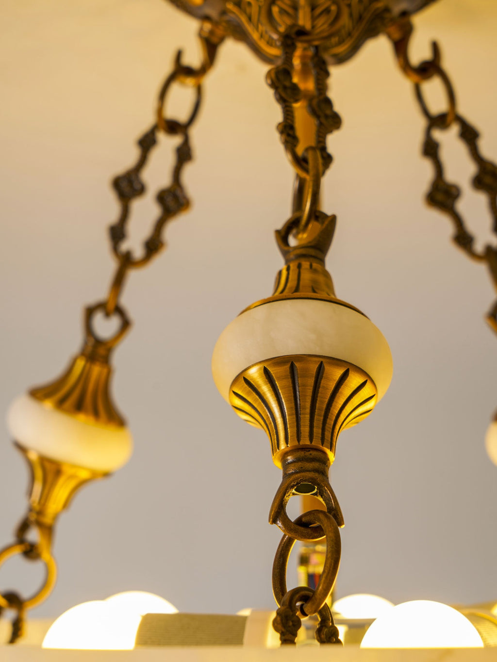 Close view of an alabaster finial, brass chain links and exposed bulbs inside this Clérachic ceiling light.