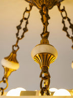 Close view of an alabaster finial, brass chain links and exposed bulbs inside this Clérachic ceiling light.