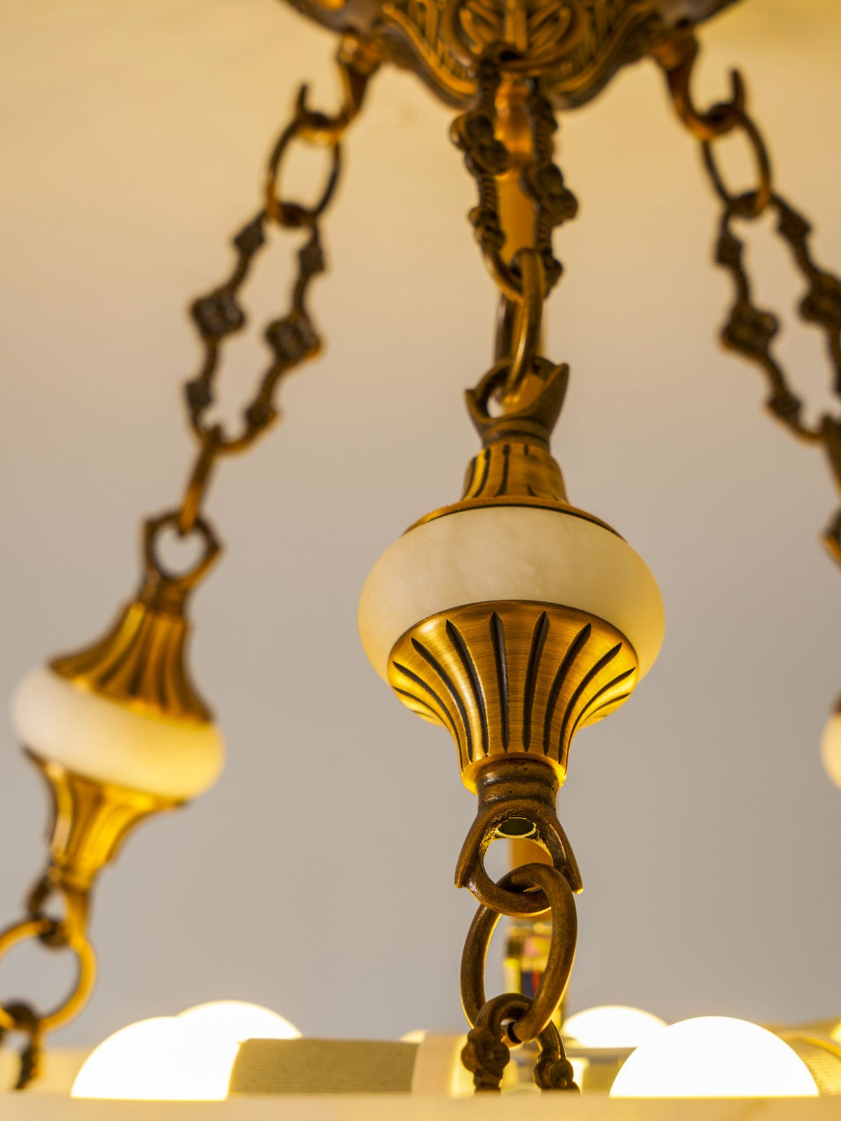 Close view of an alabaster finial, brass chain links and exposed bulbs inside this Clérachic ceiling light.